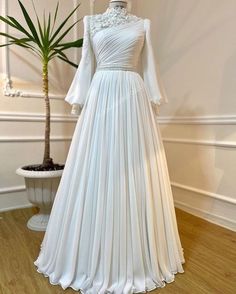 a white wedding dress on display in a room with a potted plant and mirror