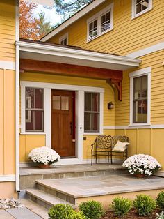 a yellow house with white flowers on the front steps