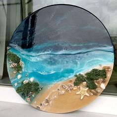 a glass plate that is sitting on a window sill next to the ocean and sand