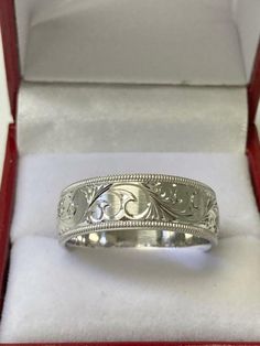 a silver ring in a red box with white paper on the bottom and an ornate design