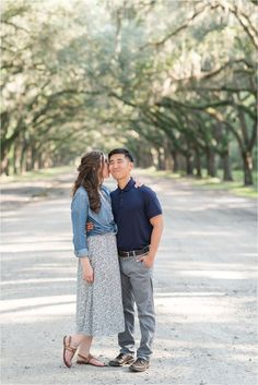 an engaged couple kissing in the middle of a road surrounded by live oak trees during their engagement session