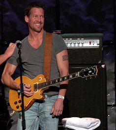 a man holding a guitar and singing into a microphone while standing in front of an amp