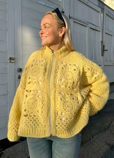 a woman standing in front of a building wearing a yellow sweater