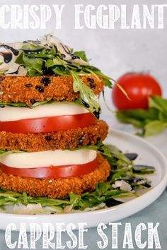 a stack of food sitting on top of a white plate next to tomatoes and lettuce