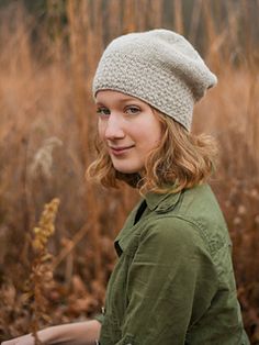 a woman standing in tall grass wearing a knitted hat