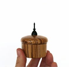 a hand holding a small wooden box with a black knob on it's top