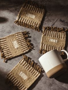 Set of four handwoven coasters with earthy tones, arranged on a rustic surface alongside a ceramic mug. Weaving Coasters Diy, African Weaving, Woven Coasters, Wool Coasters, Weaving Loom Diy, Entertaining Gifts, Best Travel Accessories, Diy Coasters, Weaving Projects