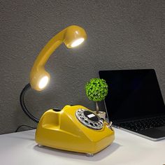 a yellow telephone sitting on top of a desk next to a laptop computer and a green tree