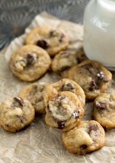 mini chocolate chip cookies on a piece of parchment paper next to a glass of milk