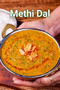 a person holding a bowl of food with the words methi dal in front of it