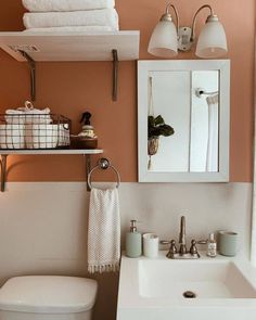 a white toilet sitting under a bathroom mirror next to a sink and a towel rack