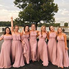 a group of women standing next to each other in long pink dresses with one woman raising her arm