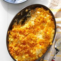 a casserole dish with cheese and other food on a table next to utensils