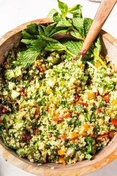 a wooden bowl filled with green vegetables and couscous on top of a white table