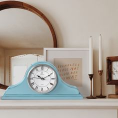 a blue clock sitting on top of a mantle next to candles and framed pictures in front of a mirror