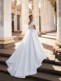 a woman in a white wedding dress standing on some steps wearing an off the shoulder gown