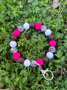 a bracelet with pink, brown and white beads on it sitting in the green grass