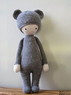 a crocheted gray teddy bear sitting on top of a wooden table next to a white wall