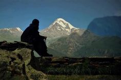 a man sitting on top of a rock next to a large mountain covered in snow