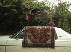 an old rug is sitting on the hood of a car in front of some pink flowers