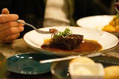 a person holding a fork over a plate of food on a table with other plates and utensils