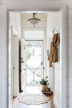 an open door leading to a porch with potted plants on the floor and coat rack