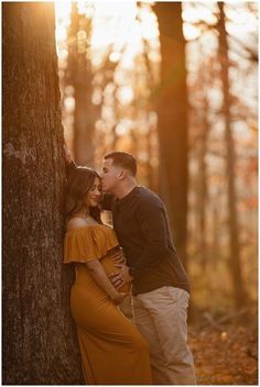 a couple cuddles against a tree in the woods at sunset during their engagement session