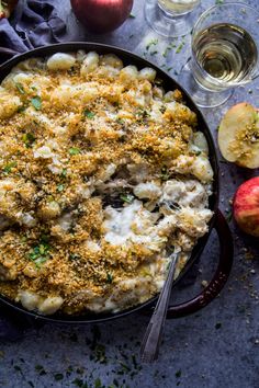 an apple and cheese casserole in a pan with two glasses of wine on the side