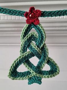 a crocheted christmas tree ornament hanging from a string with a red flower on top