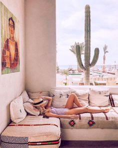 a woman laying on top of a white couch next to a large cactus in a living room