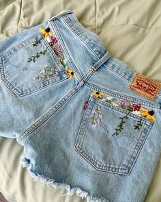 a pair of jean shorts with embroidered flowers on the front and back, sitting on a bed