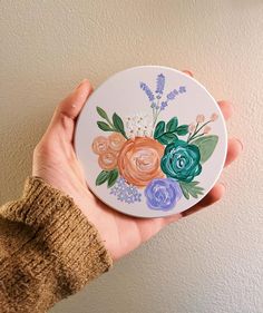 a hand holding a plate with flowers painted on it