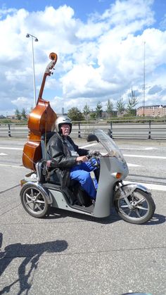 a man riding on the back of a motorcycle next to a double bass guitar case