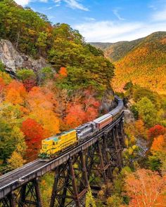 a train is going over a bridge in the mountains with trees turning orange and yellow