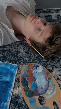 a young man laying on the floor next to an easel and painting palettes