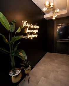 there is a neon sign on the wall next to two potted plants