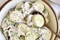 a white bowl filled with potato salad on top of a table next to a fork