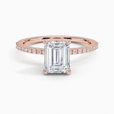 an emerald cut engagement ring with diamonds on the band and side stones in yellow gold