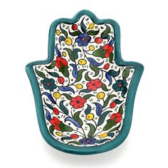 a ceramic hamsa with colorful flowers and leaves on the front, hanging from a wall