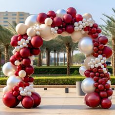 a red and white balloon arch in the middle of a walkway with palm trees behind it