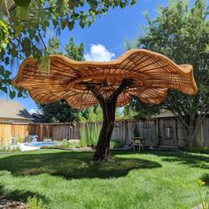 a large wooden umbrella sitting on top of a lush green field next to a tree