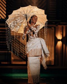 a woman in a white dress holding an umbrella and smiling at the camera while standing on stage