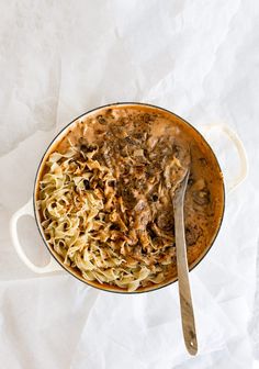 a large pot filled with pasta and meat on top of a white table next to a spoon