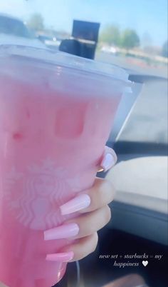 a woman's hand holding a pink drink in a cup with the lid up