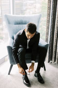 a man in a suit and tie tying his shoelaces while sitting on a chair