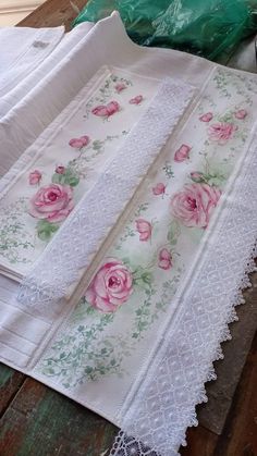 several pieces of white lace with pink roses on them sitting on top of a wooden table