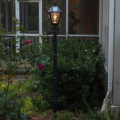 a lamp post in front of a house with roses growing around it and an open window