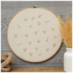 a white wall hanging with pink flowers and green leaves on it next to a vase