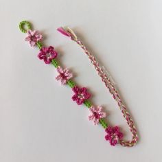 a pink and green crochet bracelet with flowers on it, sitting on a white surface