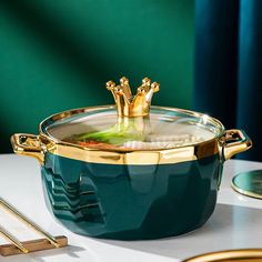 a green pot with a gold crown sitting on top of it next to some forks and spoons